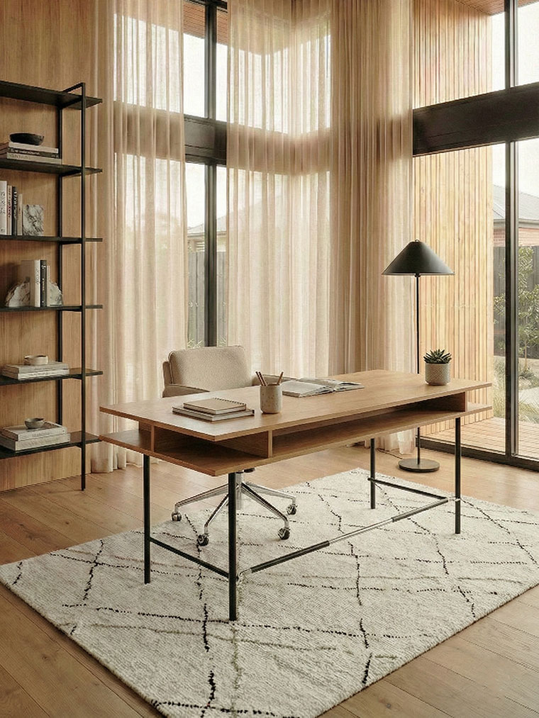 Minimalist home office with a light wood desk and black metal frame, positioned in a glass corner overlooking the garden with airy linen drapes.