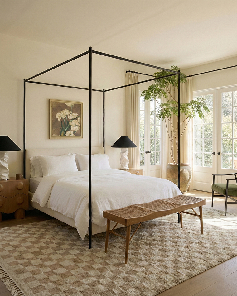 Contemporary earth-toned bedroom with black canopy bed, white linen bedding, checkerboard rug and olive accent chair