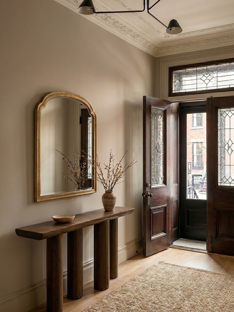 Classic townhouse entryway with historic stained-glass double doors, a sculptural wood console table with cylindrical legs, and a vintage gold arched mirror.